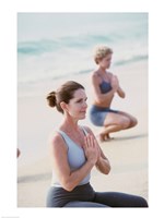 Young woman and a mid adult woman meditating on the beach Fine Art Print
