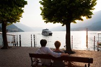 Couple sitting on bench and watching ferry approaching dock along the Lake Como, Bellagio, Province of Como, Lombardy, Italy Fine Art Print