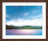 Pink light cast down on two rings in lavender water with deep blue sky and clouds over green mountains in distance Fine Art Print