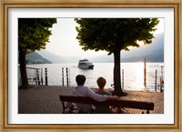 Couple sitting on bench and watching ferry approaching dock along the Lake Como, Bellagio, Province of Como, Lombardy, Italy Fine Art Print