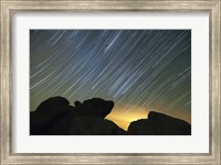 Light pollution illuminates the sky and star tails above large boulders Fine Art Print