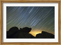 Light pollution illuminates the sky and star tails above large boulders Fine Art Print