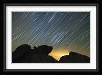 Light pollution illuminates the sky and star tails above large boulders Fine Art Print