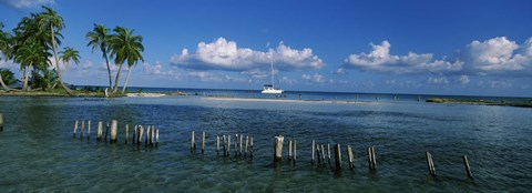 Framed Wooden posts in the sea with a boat in background, Laughing Bird Caye, Victoria Channel, Belize Print