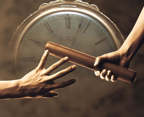 Framed Close up of two runners hands passing the baton in relay race in front of old European clock face Print