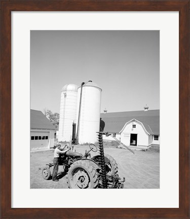 Framed USA, Farmer Working on Tractor, Agricultural Buildings in the Background Print