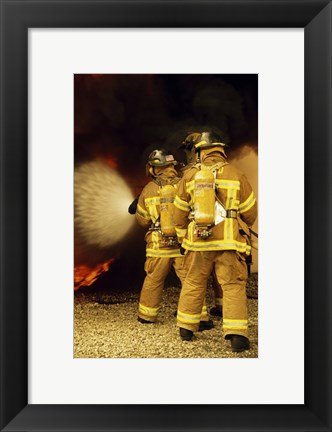 Framed Rear view of three firefighters extinguishing a fire Print