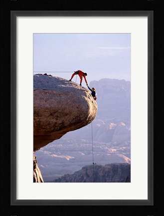 Framed Side profile of a young man pulling a young woman onto a rock Print