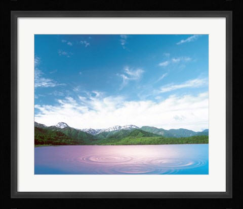 Framed Pink light cast down on two rings in lavender water with deep blue sky and clouds over green mountains in distance Print