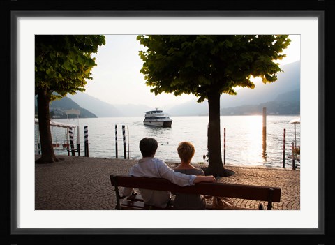 Framed Couple sitting on bench and watching ferry approaching dock along the Lake Como, Bellagio, Province of Como, Lombardy, Italy Print