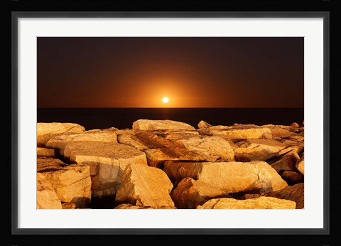 Framed moon rising behind rocks lit by a nearby fire in Miramar, Argentina Print